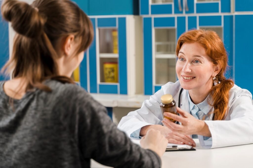 A doctor holding an open jar of medication or supplements, smiling and consulting with a female patient across a desk with blue shelving in the background.